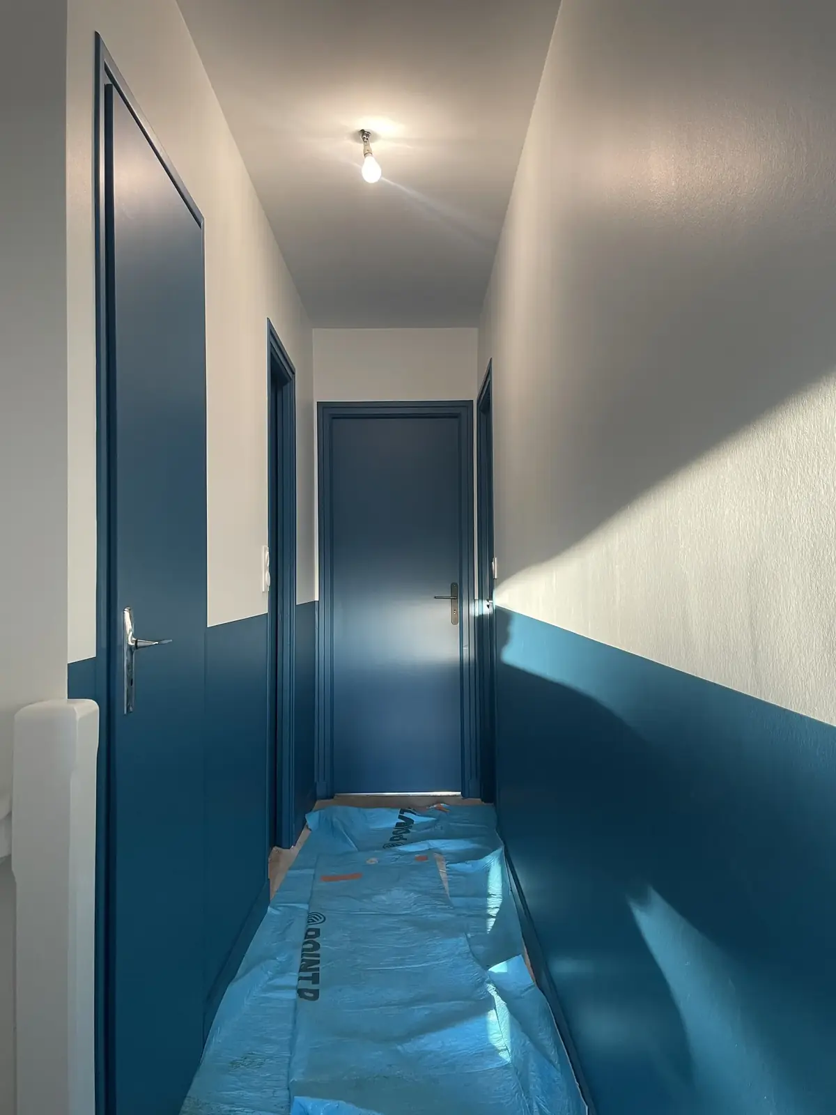 Couloir de l’étage à Belz, portes et soubassement en teinte soutenue, sol protégé par un film