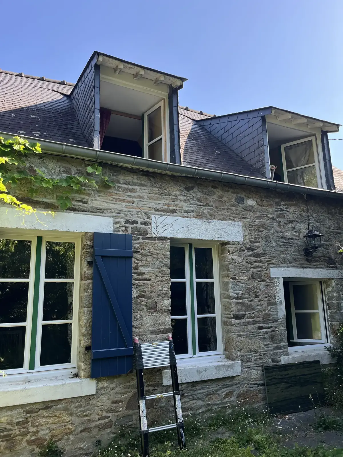 Longère de Peillac pendant le chantier, échelle dressée contre la façade, volets bleus et lucarnes en ardoise