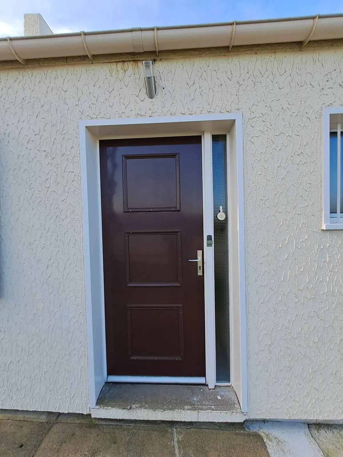 Porte d’entrée en bois ton soutenu sur une façade à enduit projeté remise en blanc, à Pleucadeuc