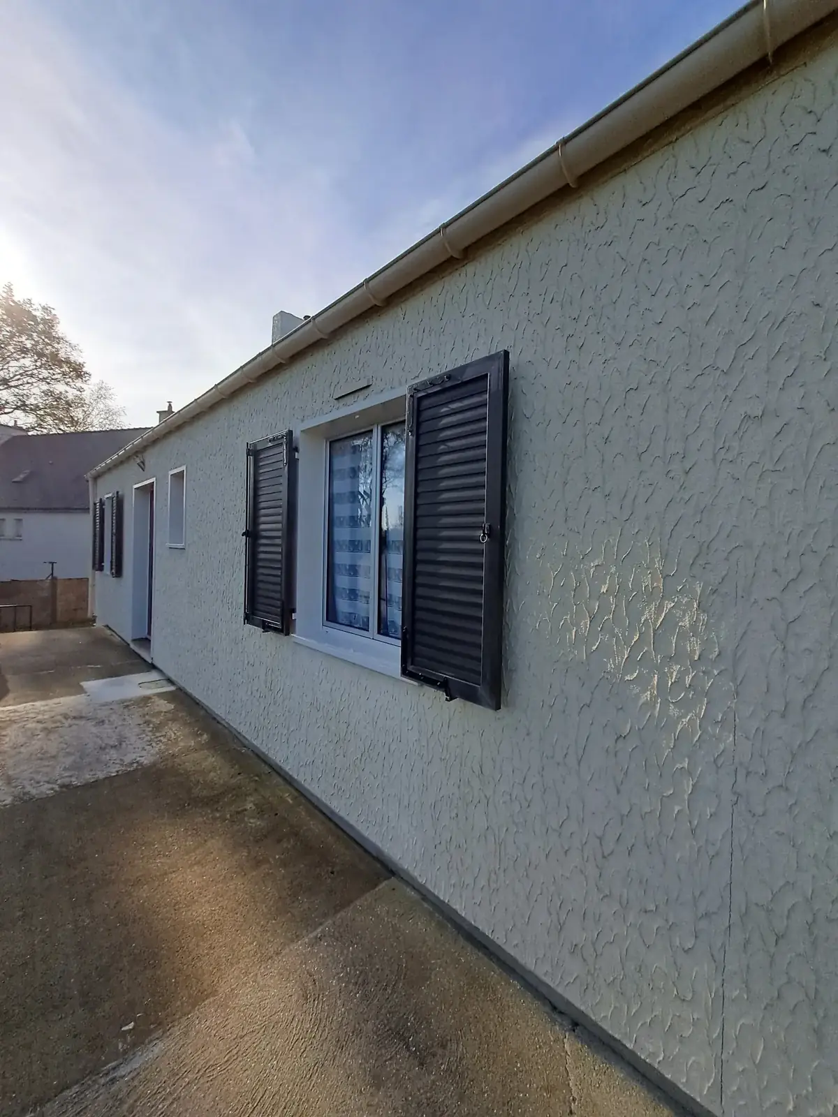 Façade latérale d’une maison de Pleucadeuc, enduit clair à relief et volets en ton soutenu