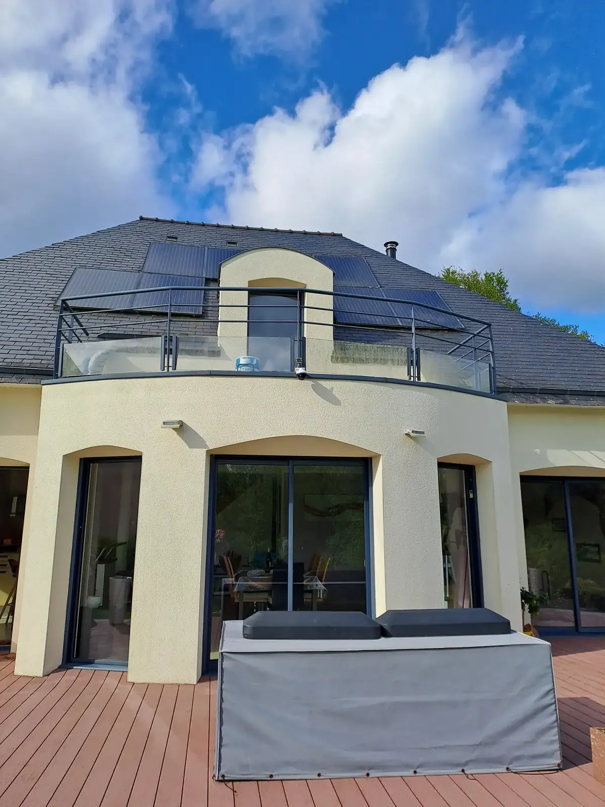 Façade sur terrasse d’une maison contemporaine de Tréffléan après mise en peinture, enduit crème, balcon courbe et couverture en ardoise