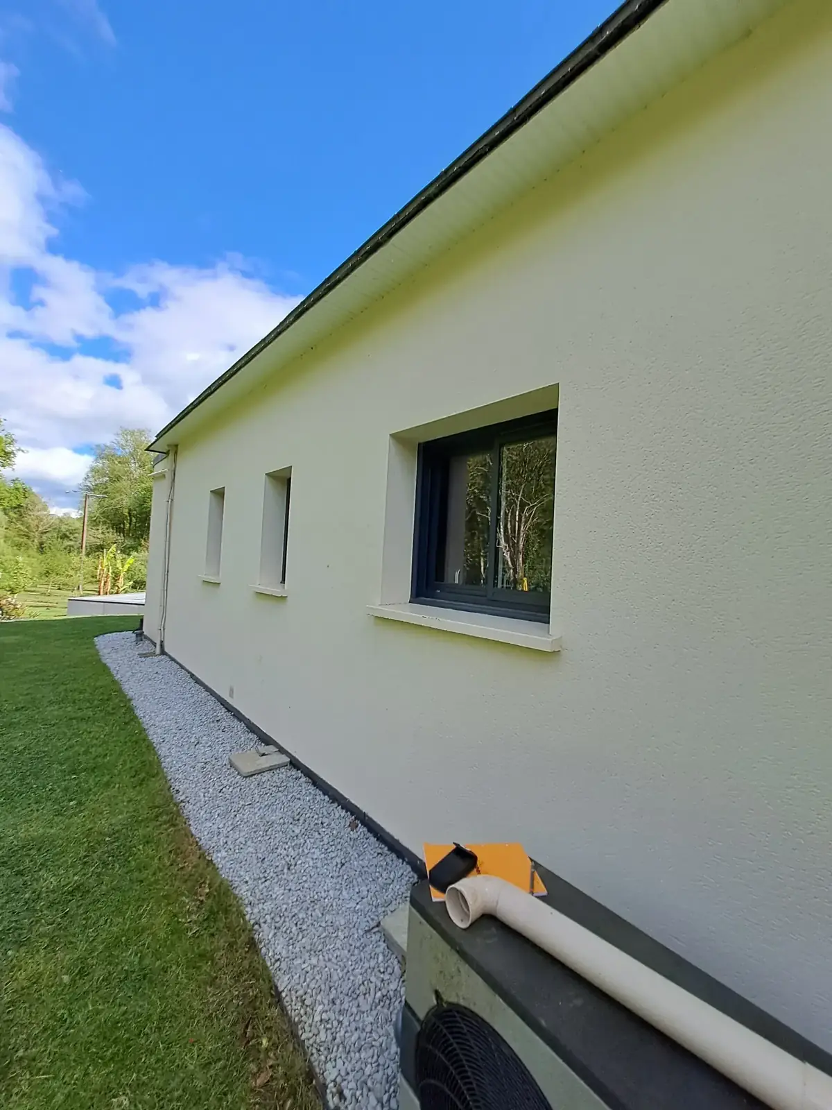 Long mur d’une maison de Tréffléan après mise en peinture, enduit crème, menuiseries anthracite et bande de gravier en pied de mur