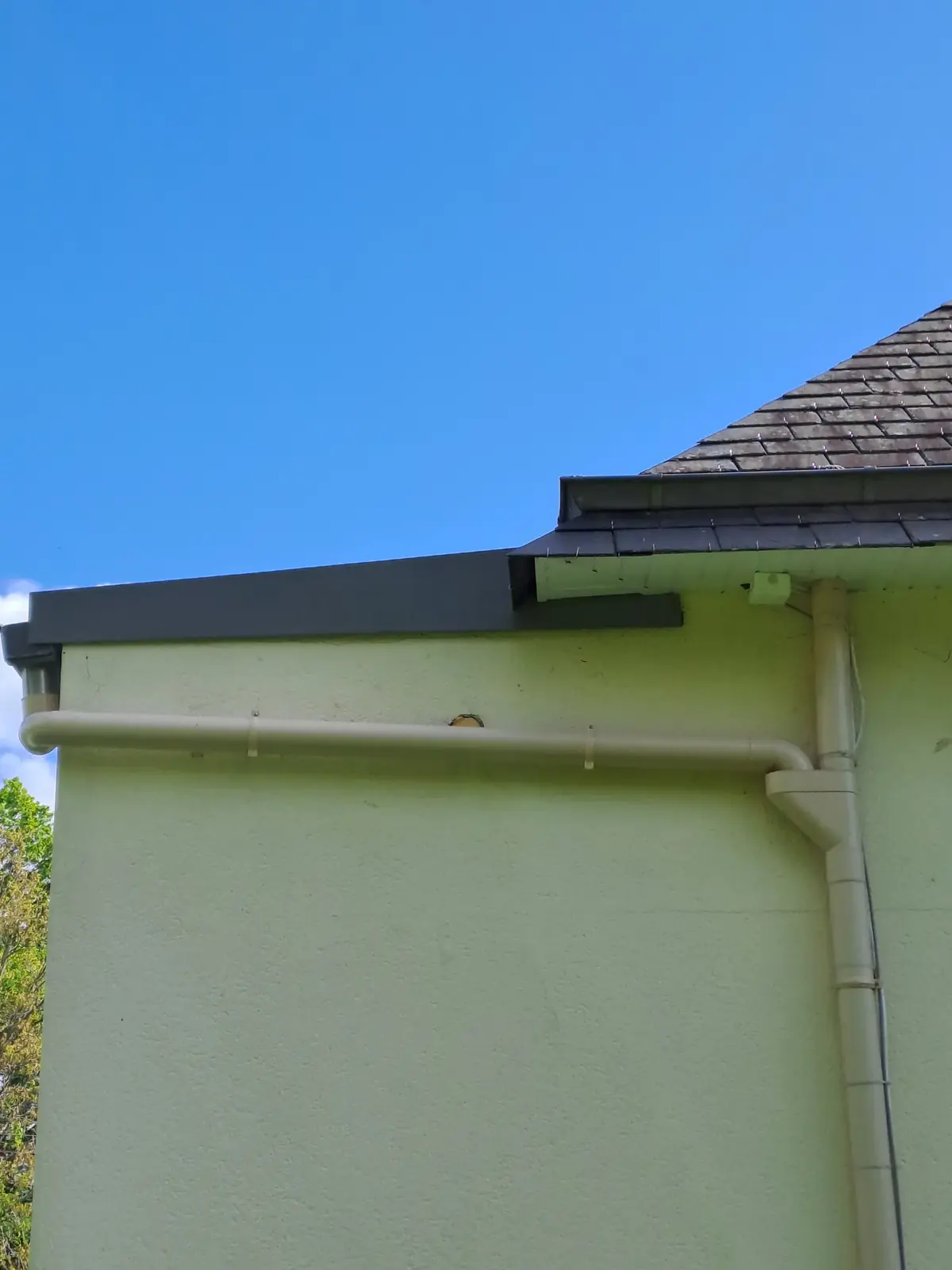 Angle d’une maison de Tréffléan, débord de toit, gouttière et descente d’eau pluviale au-dessus de l’enduit peint