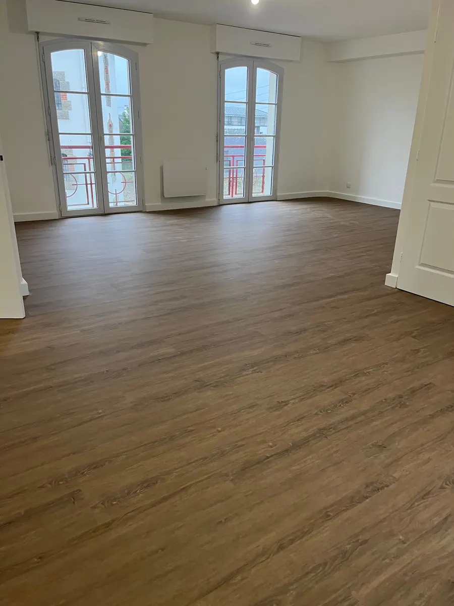 Séjour d’un appartement de Vannes après chantier, portes-fenêtres cintrées, murs blancs et sol souple en lames