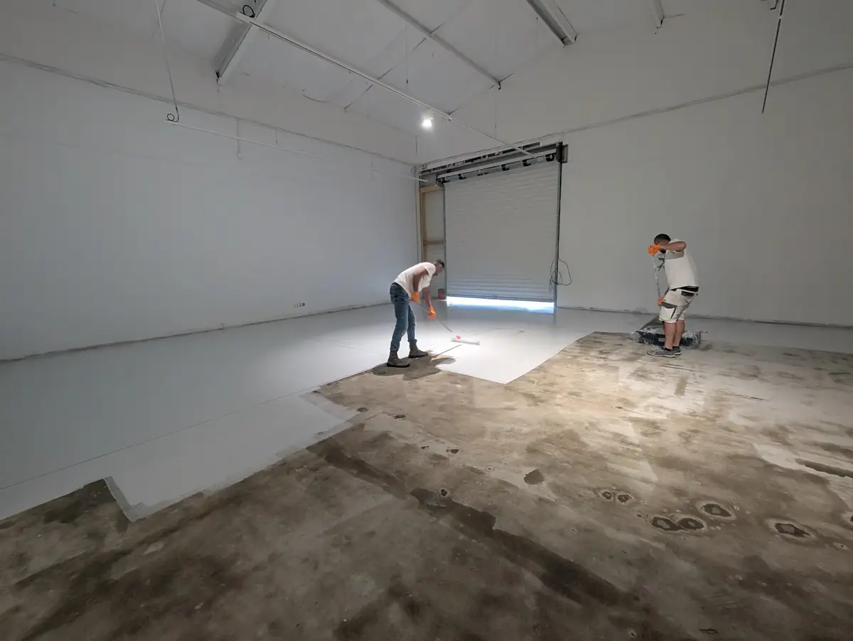 Sol d’atelier à moitié traité&nbsp;: béton encore brut d’un côté, couche d’accroche posée de l’autre