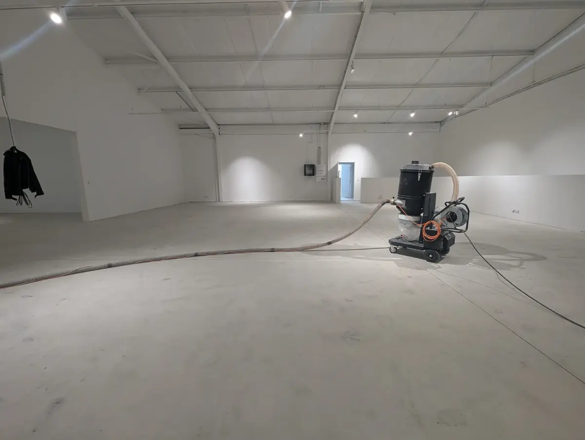 Aspirateur industriel et son flexible dans un hall d’atelier, béton préparé